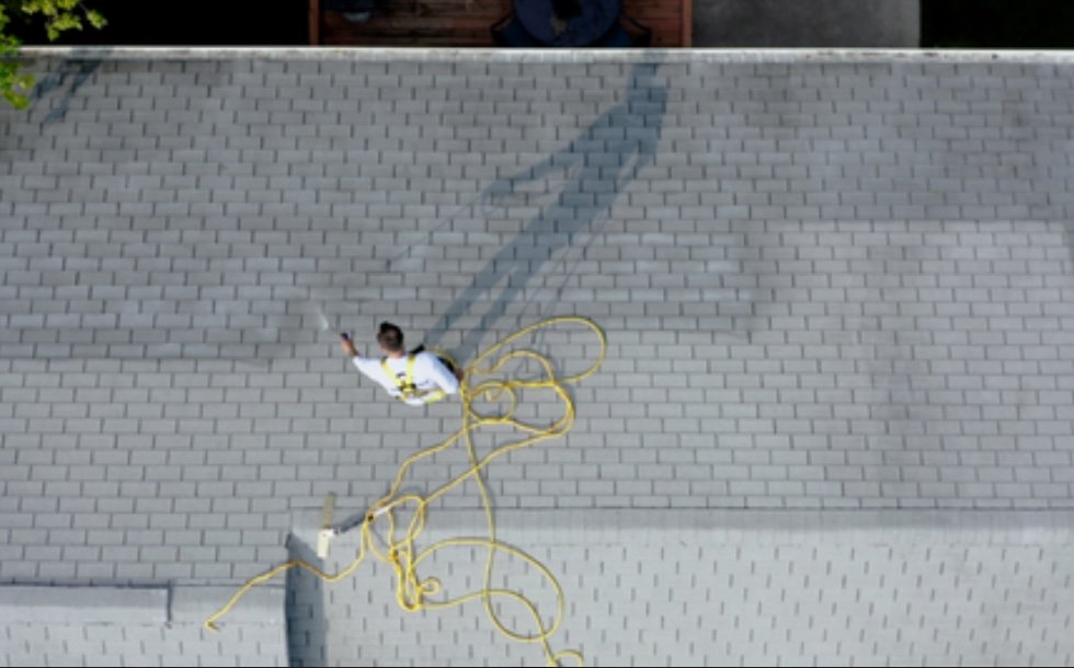 Aerial view of worker spraying GreenSoy treatment on roof with professional equipment